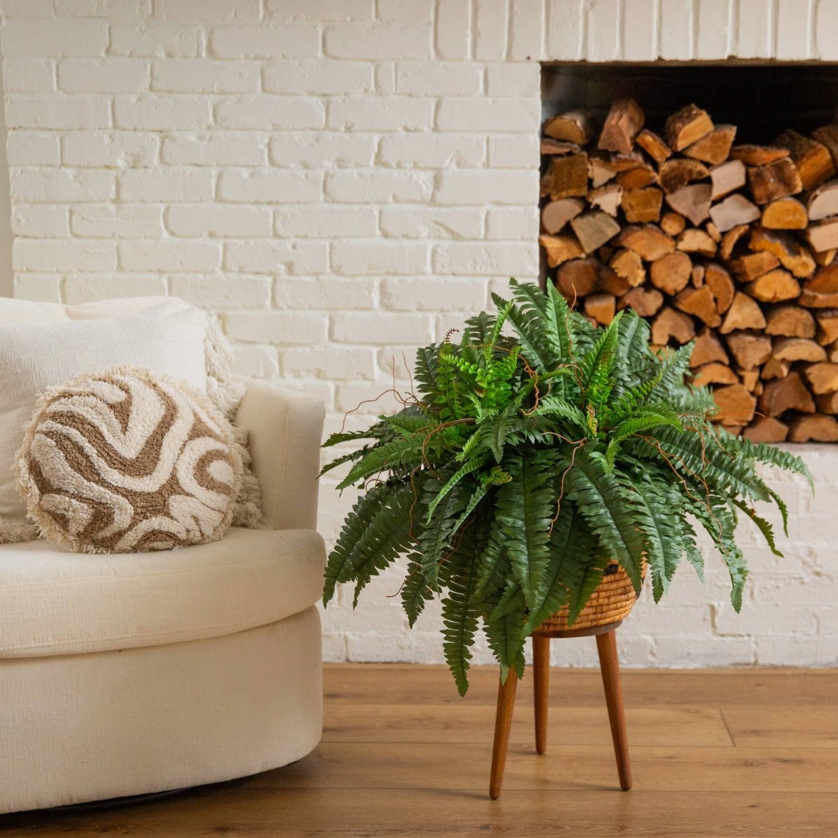 Living room with beige sofa, potted artificial fern, and stacked firewood against a white brick wall.