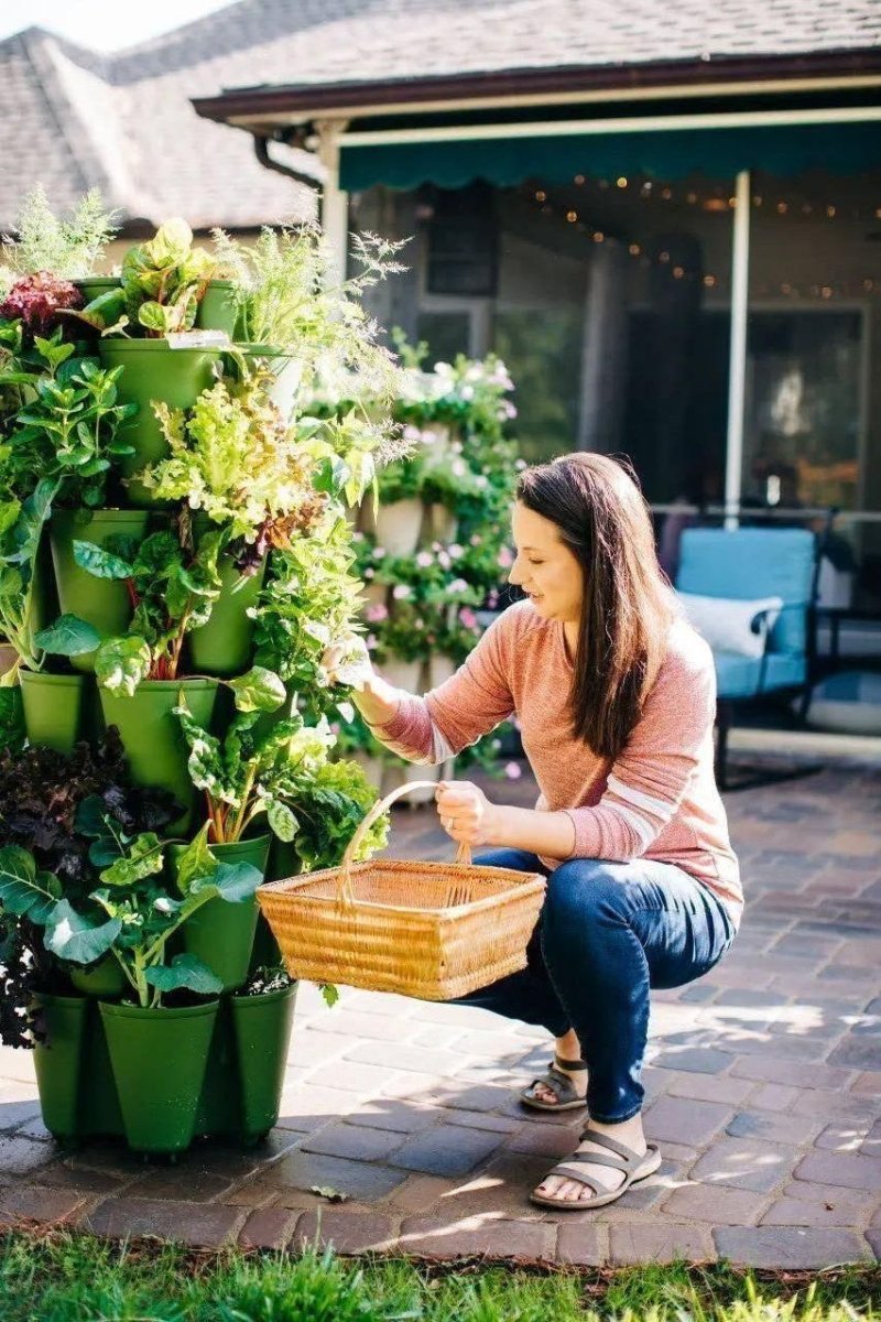 Woman tending to a vertical Greenstalk garden with potted plants on a patio.