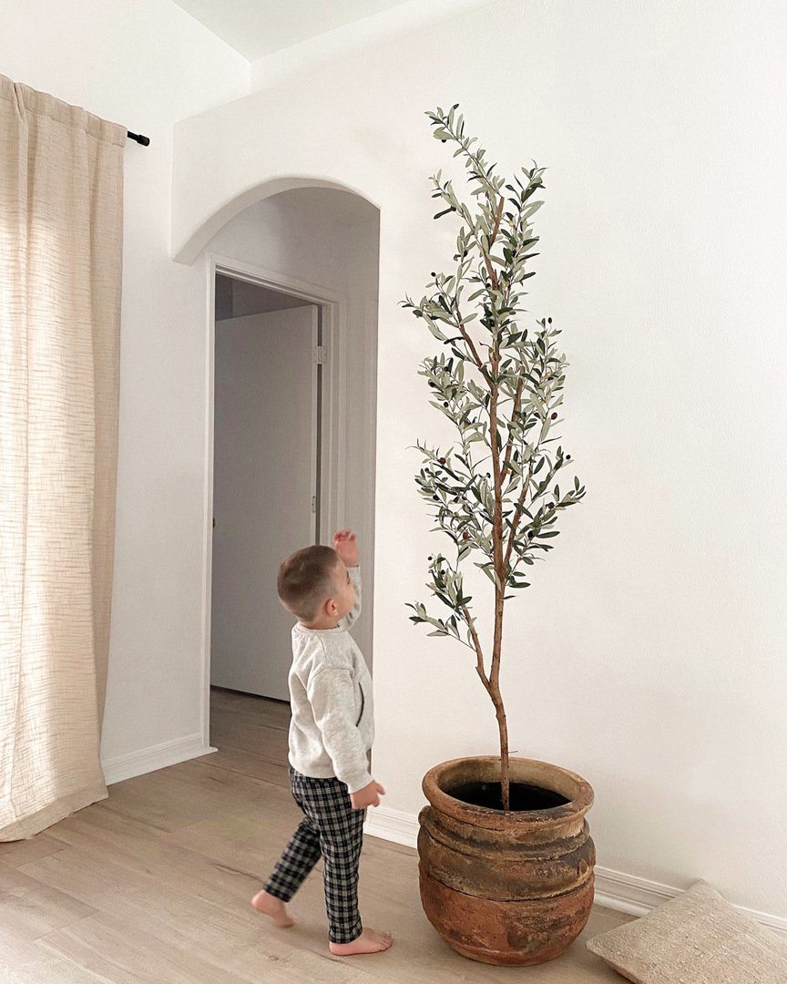 Child standing next to 82" Artificial Olive Tree for height comparison