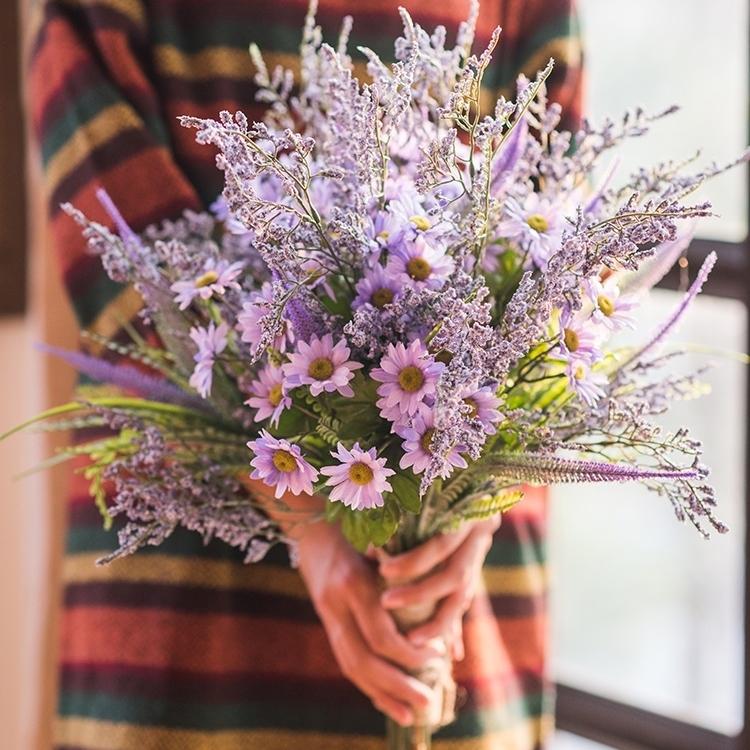 Person holding a bouquet of purple flowers with a colorful striped garment.