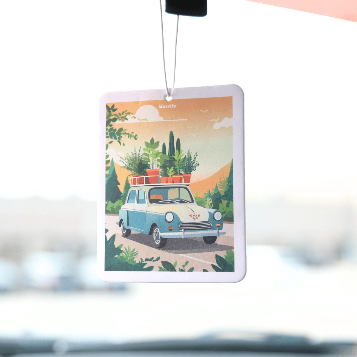 Car air freshener with a scenic design of a car and plants hanging from a car's rearview mirror.