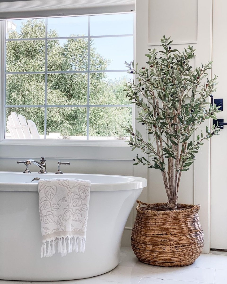 Bathroom with freestanding bathtub, towel, and potted artificial plant near a window.