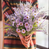 Person holding a bouquet of purple flowers with a colorful striped garment.