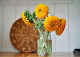 Clear glass vase with bright yellow sunflowers on a wooden surface with a woven basket in the background.
