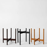 Three minimalist plant stand designs in different colors on a white background
