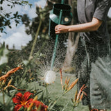 Person watering plants with a green Haws watering can in a garden
